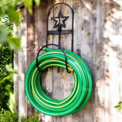 Green garden hose coiled on a wall-mounted holder with a star design against a wooden background.